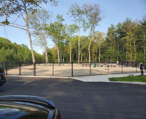 A black car is parked in a parking lot with a playground in the background.