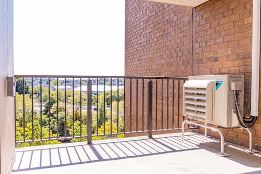 A balcony with a brick wall and a white air conditioning unit.
