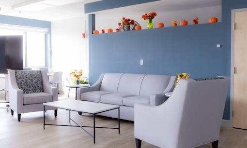 Community Room seating with a grey sofa, a grey armchair, and a small table with flowers.