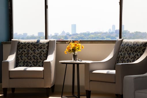 Community Room seating with a view Two chairs and a table with flowers on it in front of a window with a city view.