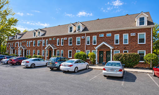 A parking lot in front of a red brick building with cars parked.
