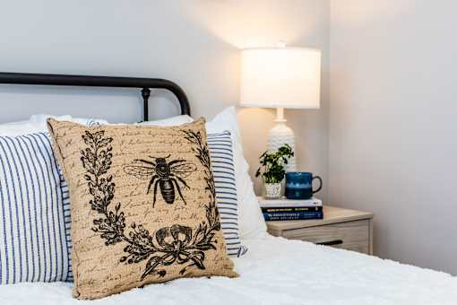 A bed with a bee design on the pillow and a lamp on the side table.