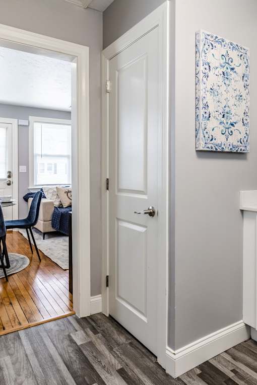 A white door is open to a room with a blue chair and a blue and white picture on the wall.