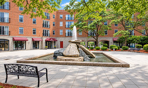 A fountain in the middle of a courtyard surrounded by benches and trees.