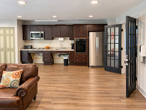 A brown leather couch sits in a kitchen with dark wood floors and white walls.