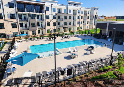 A large swimming pool surrounded by a black fence and lounge chairs.