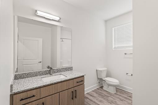 A bathroom with a sink, mirror, toilet and wooden cabinets.