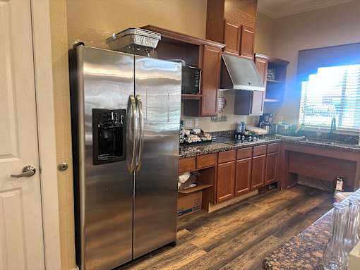 A stainless steel refrigerator stands in a kitchen with wooden cabinets and a rug on the floor.