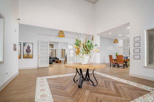 A room with a round table and chairs, a vase with flowers, and pictures on the wall.