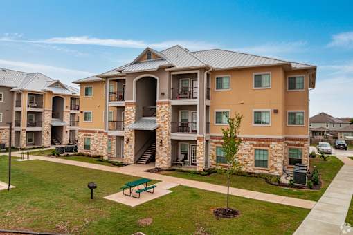 Apartment complex with a green lawn and a tree in front.