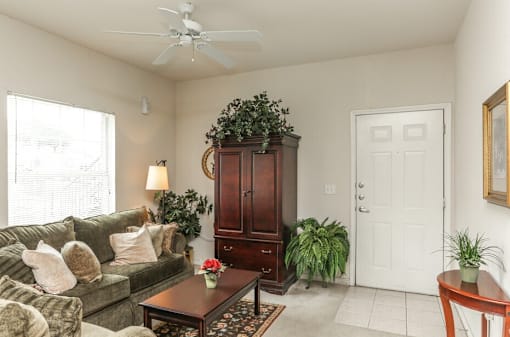 A living room with a couch, a coffee table, a plant, and a cabinet.
