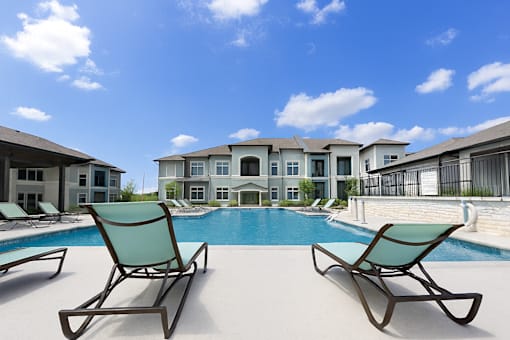 A pool with two chairs in front of a building.