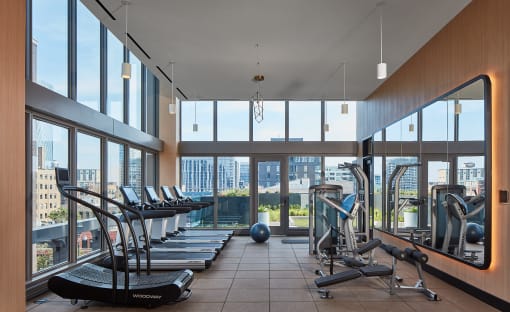 a gym with treadmills and weights with a view of the city