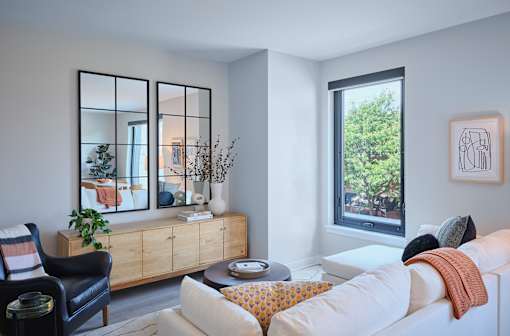 A living room with a white couch, a black chair, and a wooden cabinet with a mirror above it.