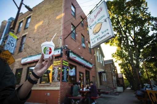 A person holding a cup of food in front of a building.