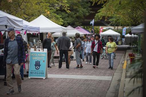A group of people walking through a market with a sign that says "Kool Karma Bracelets".