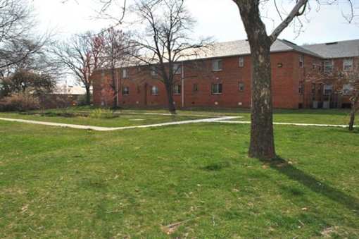 A large red brick building with a white fence and a tree in front.