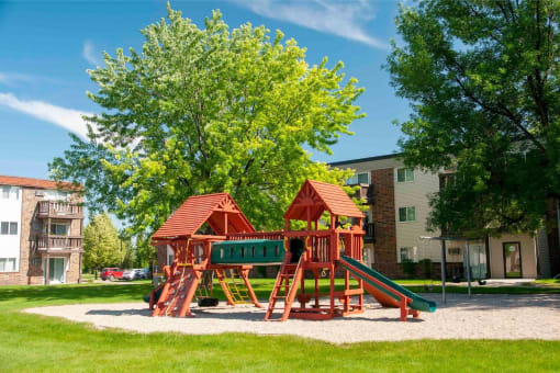 a playground in the middle of a yard with trees and apartment buildings