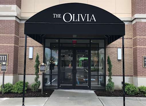 The entrance to a building named The Olivia with a black awning at The Olivia Apartments, Carmel, Indiana