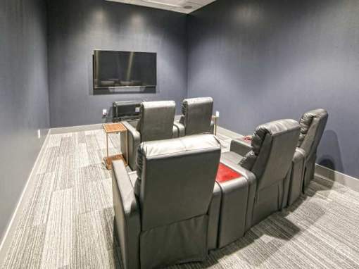 A row of grey recliner chairs are lined up in front of a television at The Olivia Apartments, Carmel 46032