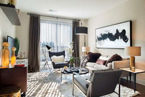 A living room with a grey couch, a black chair, and a large abstract painting on the wall at The Olivia Apartments, Carmel