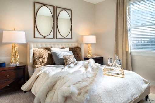A bedroom with a large bed covered in a white fur throw at The Olivia Apartments, Indiana