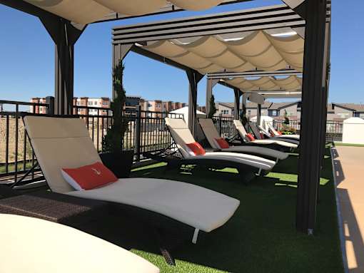 A row of sun loungers are arranged on a green carpet under a striped awning at The Olivia Apartments, Carmel, IN, 46032