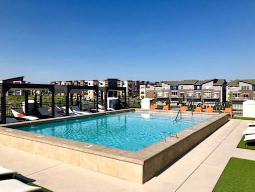A swimming pool surrounded by lounge chairs and apartment buildings in the background at The Olivia Apartments, Indiana, 46032