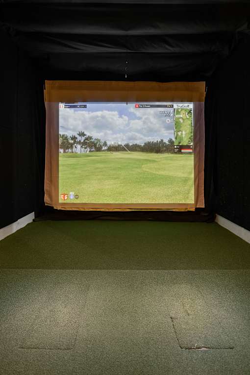 A golf course is displayed on a screen in a dark room.