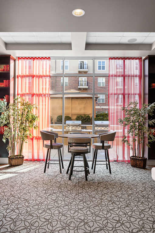 A dining room with a table and chairs in front of a window with red curtains.