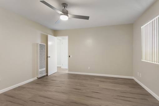 A room with a ceiling fan and light, hardwood floors, and a door with a window.