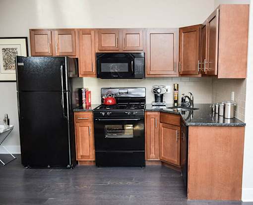 A black refrigerator stands next to a black stove in a kitchen with wooden cabinets.