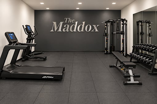 A gym with a treadmill, weights, and a wall that says The Maddox.
