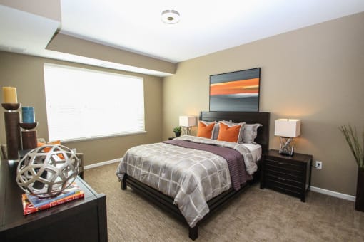 a bedroom with a bed and nightstand with a lamp on top of it at The Flats at Cedar Grove, Eagan, MN, 55122