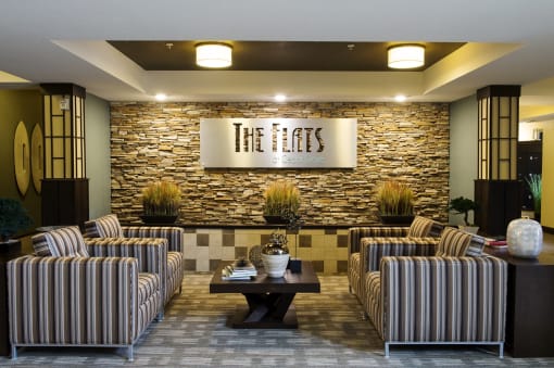 a lobby with striped chairs and a coffee table in front of a stone wall at The Flats at Cedar Grove, Eagan, Minnesota