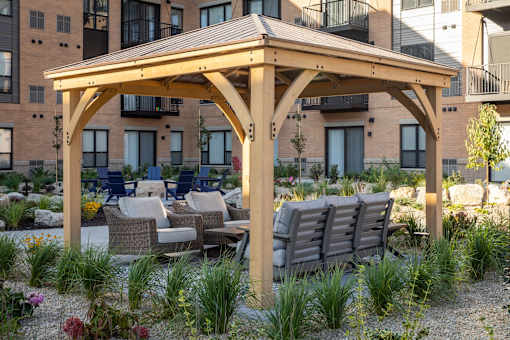 a wooden pavilion with a seating area and a fire pit in front of an apartment building at The Gallery Apartments, Burnsville, MN