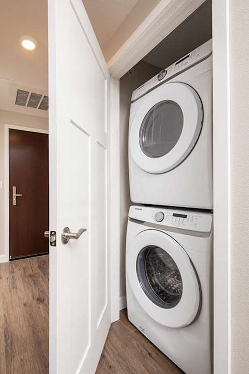 A white dryer is stacked on top of a white washer in a small laundry room.