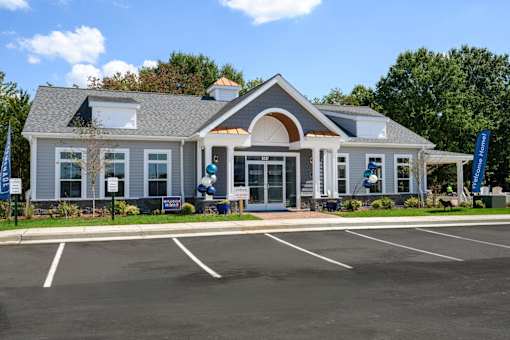 A building with a grey roof and white walls with a parking lot in front at The Promenade at Easton Apartments, Easton, 21601
