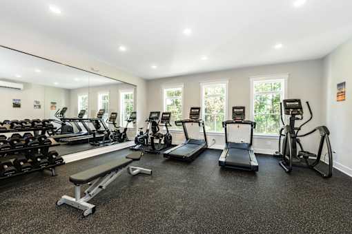 A gym with treadmills, elliptical machines, and dumbbells at The Promenade at Easton Apartments, Easton Maryland
