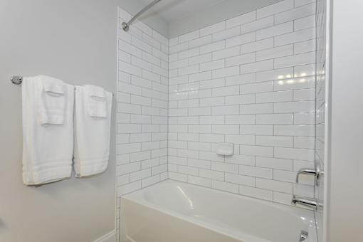 A white tiled bathroom with a white tub and towel racks at The Promenade at Easton Apartments, Easton