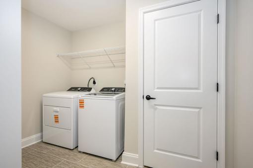 A white door is open to a room with two white washing machines at The Promenade at Easton Apartments, Maryland, 21601