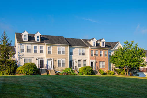 a row of houses on a green lawn with a blue sky at Townes at Village Center Apartments, Reisterstown, 21136