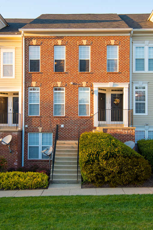 the front of a brick apartment building with stairs and a lawn at Townes at Village Center Apartments, Reisterstown, 21136
