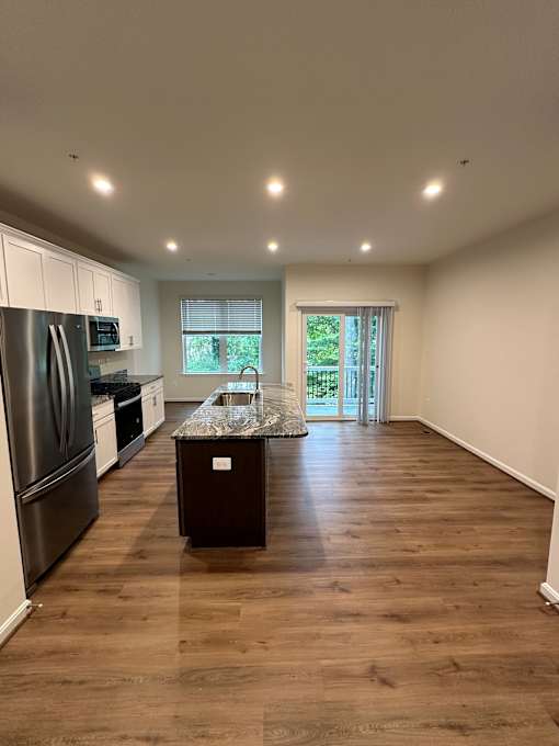 A kitchen with a refrigerator, microwave, and a wooden floor.