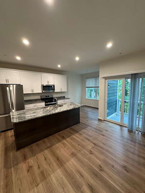 A kitchen with a refrigerator, microwave, and oven on a marble countertop.