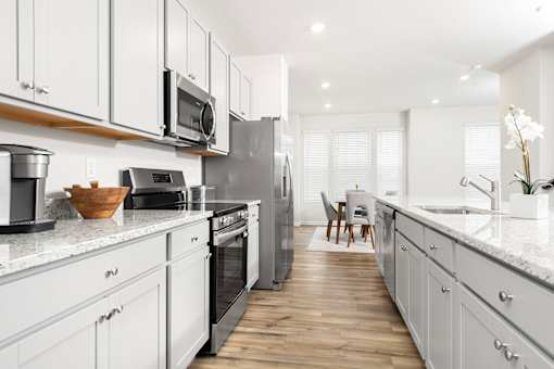 A modern kitchen with white cabinets and stainless steel appliances.at Forge Overlook, Halethorpe
