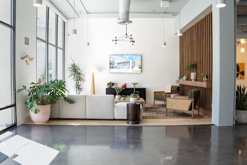 A modern office lobby with a large white sofa, a wooden side table, and a TV mounted on the wall.