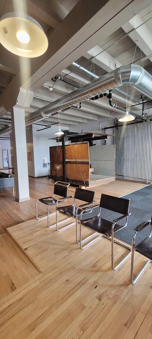 A wooden floor with a long table and chairs under a metal pipe.