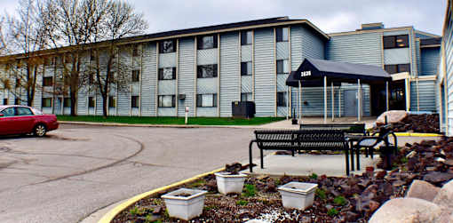 A red car is parked in front of a grey building.