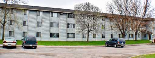 A grey apartment building with cars parked in front.